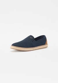 Scarpa slip-on in mesh blu navy con un accento in pelle beige sul tallone e una suola in corda naturale, caratterizzata da una superficie texturizzata e un dettaglio con logo rotondo.