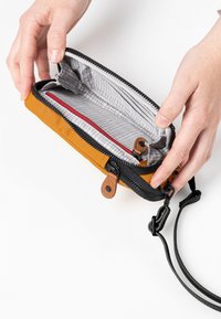 Reißverschluss-Wallet in Senfgelb mit schwarzen Akzenten. Graues gemustertes Innenfutter, verfügt über zwei Fächer und Lederdetails für die Befestigung.