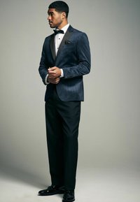 Marineblauer Samt-Tuxedo-Jacke mit satinierter Revers und schwarzen Anzughosen. Ausgestattet mit einem weißen Dress-Shirt und einer schwarzen Fliege, sauberes Design.