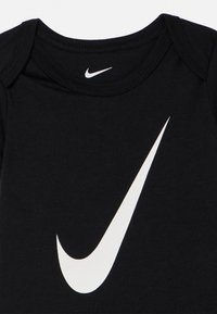 Body para bebé preto com um grande logótipo branco da Nike em formato de swoosh centrado na frente e um swoosh menor dentro da gola.