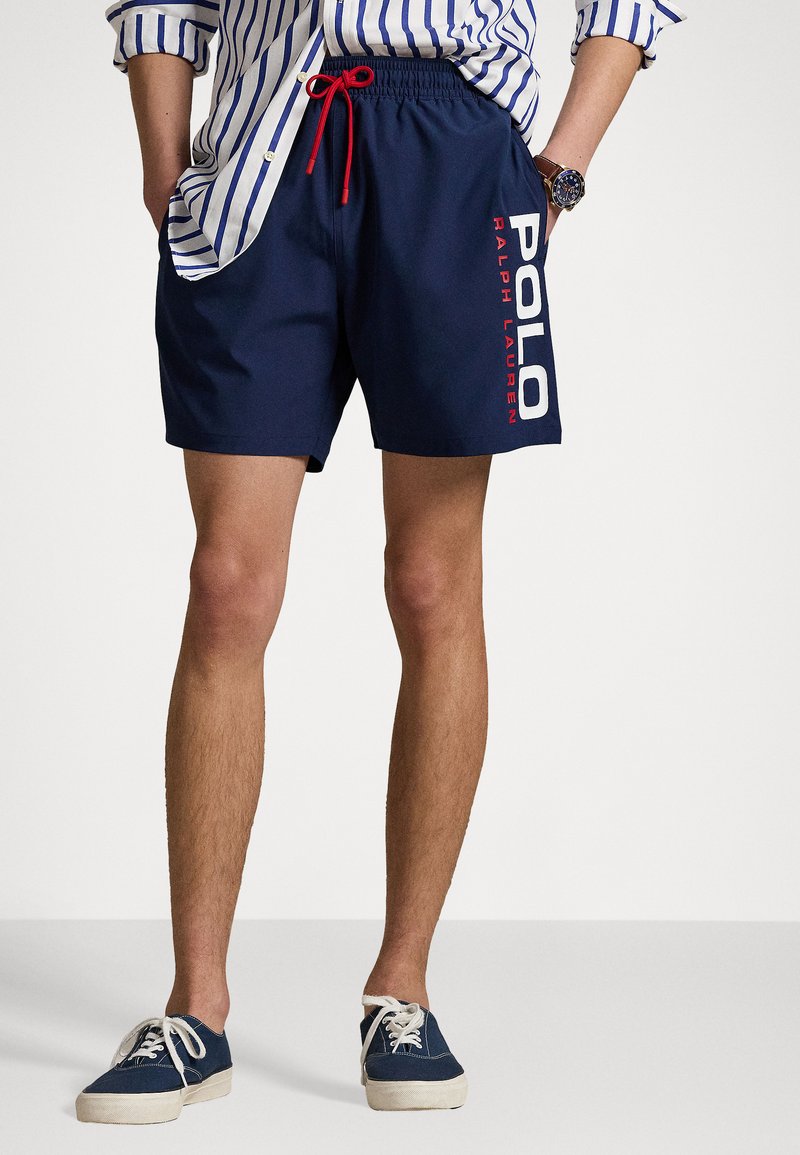 Tengerészkék úszónadrág piros zsinórral; bal oldalon fehér és piros "POLO RALPH LAUREN" logó található; sima textúrájú.