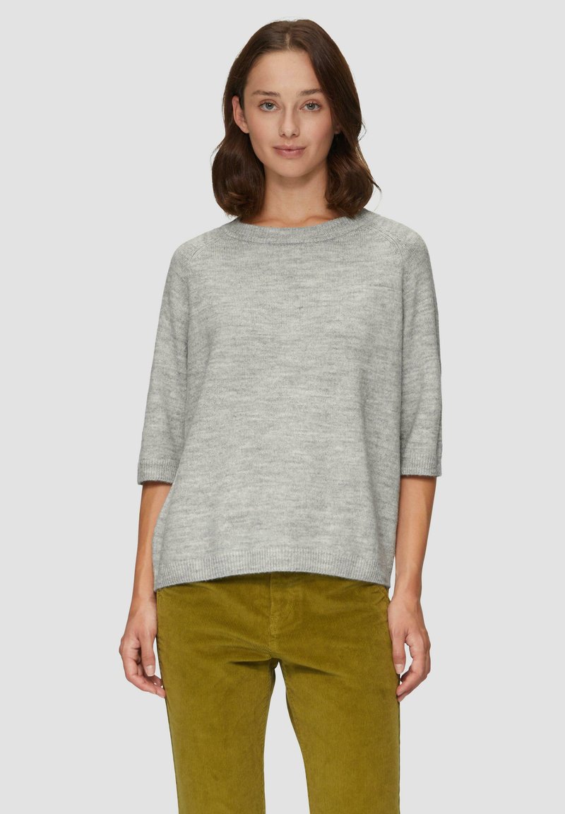 Hellgrauer Strickpullover mit rundem Halsausschnitt und Dreiviertelärmeln, kombiniert mit olivgrünen Cordhosen.