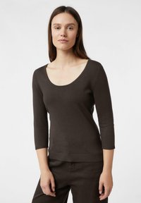 Braunes, enganliegendes Langarmshirt mit Rundhalsausschnitt und geripptem Saum, hergestellt aus einem weichen, leichten Stoff. Das Modell trägt passende Hosen.