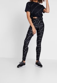 Svart tränings t-shirt med knuten framsida, ihop med svarta leggings med ett mönster av vit text. Texturerat tyg, sportig design.