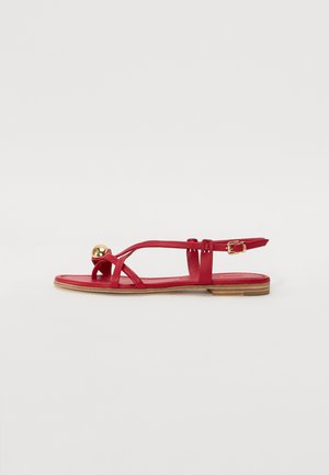 Sandales plates rouges au design minimaliste, avec des brides croisées, un accent sphérique doré et une bride de cheville à boucle.