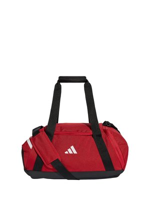 Červená sportovní taška Adidas s černými nastavitelnými popruhy a bílým logem na přední straně, navržená pro sportovní nebo cestovní účely.