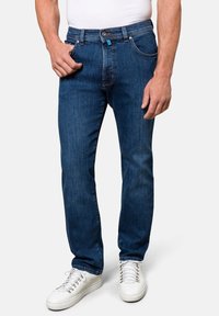 Dunkelblaue Jeans aus Denim mit geradem Schnitt, fünf Taschen und Knopfverschluss, kombiniert mit weißen Sneakers und einem schlichten weißen Hemd.