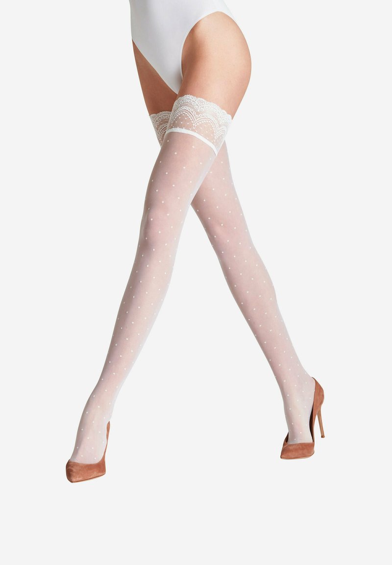 Des bas blancs transparents montant jusqu'à la cuisse avec un motif à pois et une bordure en dentelle en haut ; portés avec des chaussures à talons hauts marron.