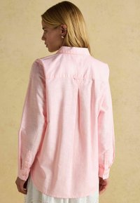 Svete ružová dlhá rukávová košeľa s textúrovanou tkaninou, manžetami na gombíky, zadným rázvorom a zaobleným lemom, prezentovaná zo zadnej bočnej strany.