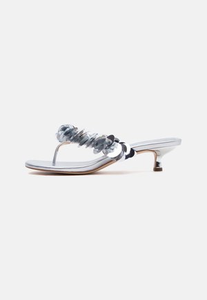 Sidabrinės aukštakulnės basutės su mažais blokuoto kulniuko ir blizgančiomis apvalių blizgučių dekoracijomis ant dirželio, priešai paprastą foną.