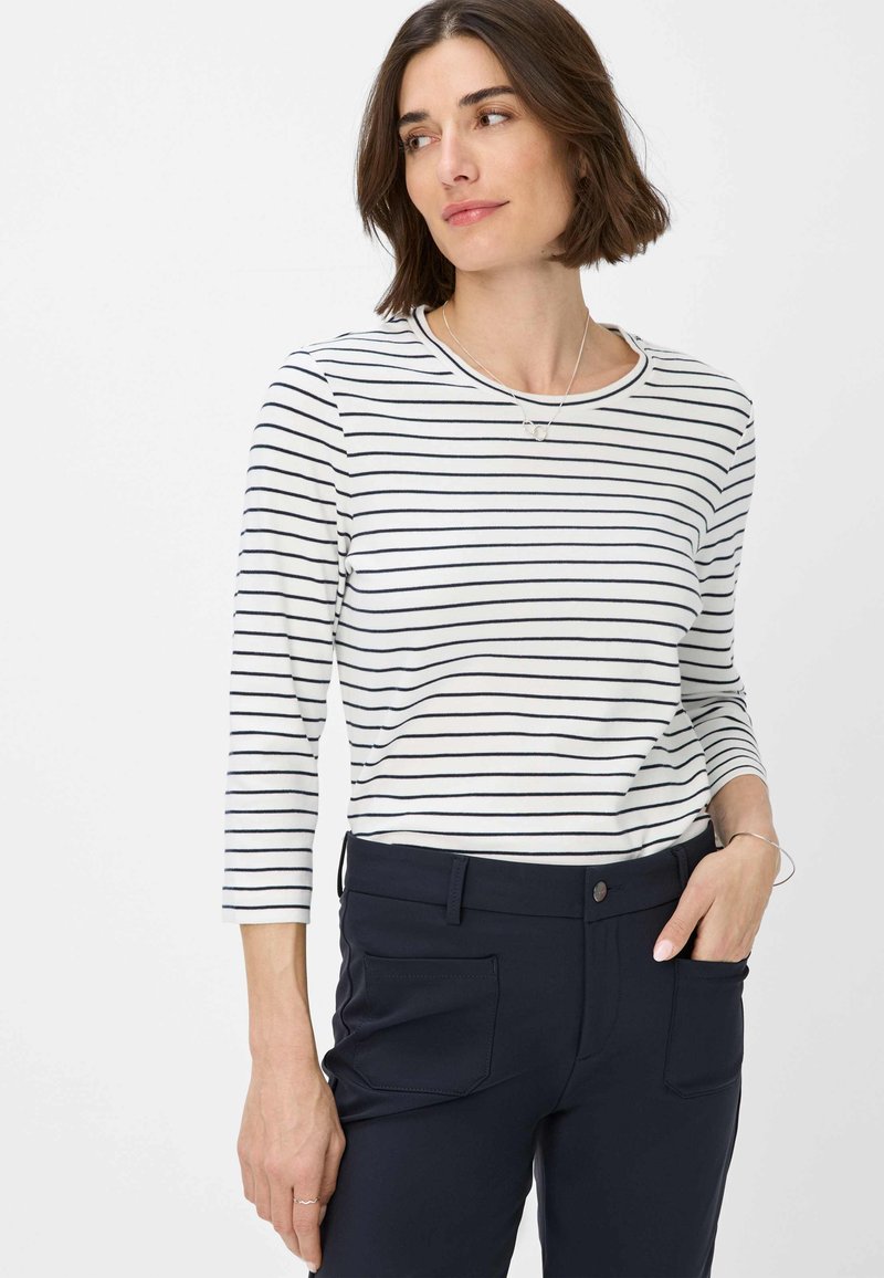 Gestreiftes langärmliges Oberteil in Weiß und Marineblau, runder Ausschnitt, leichtes Material. Kombiniert mit einer marineblauen Hose mit Seitentaschen.