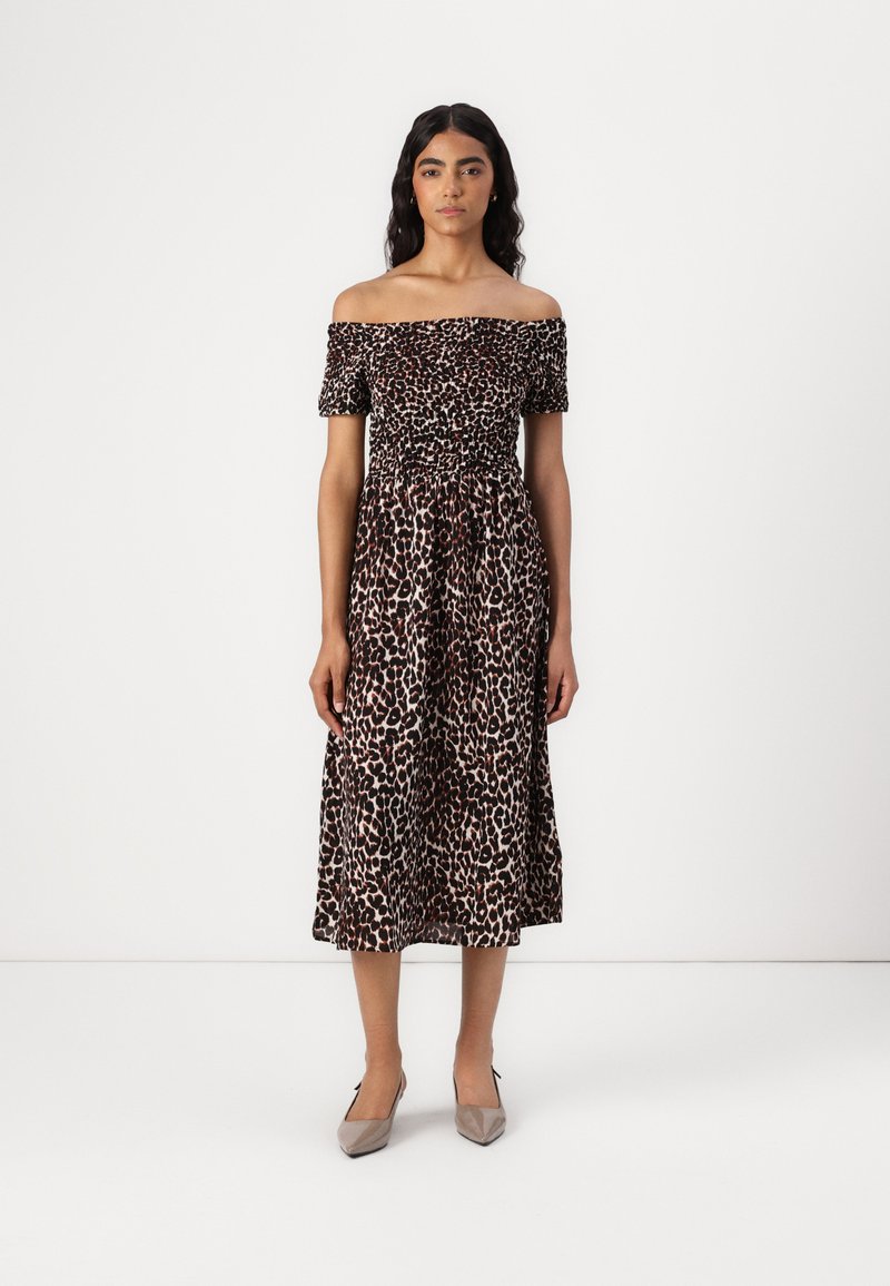 Leopardmönstrad klänning med off-shoulder-design, korta ärmar, rynkad bodice och en svängig A-linjeformad kjol, tillsammans med beige klackar.