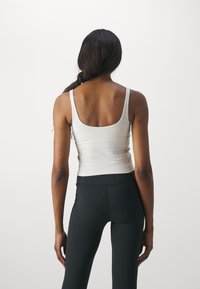 Hvit tettsittende tank topp med tynne stropper, kombinert med høytlivs svarte leggings. Glatt tekstur, rund hals og synlige sømdetaljer.