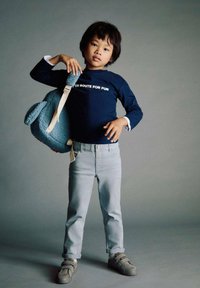 Rucsac cu ursuleț albastru, cămașă cu mânecă lungă de culoare albastru închis cu text alb, blugi de culoare albastru deschis și încălțăminte gri cu arici. Design simplu și jucăuș.