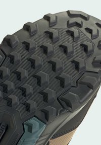 Black textured rubber sole with deep treads and traction patterns; gray and beige midsole with a light blue accent near the heel.