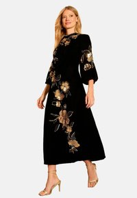 Rochie midi neagră cu mâneci clopot, cu broderie florală aurie și argintie. Textură catifelată netedă, asortată cu pantofi aurii cu barete.