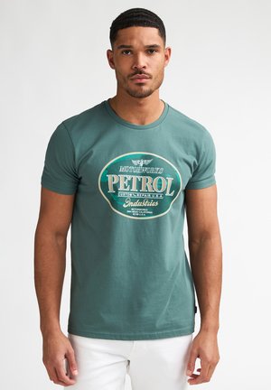 Groen katoenen T-shirt met een ronde hals en korte mouwen. Voorzijde met een grote witte opdruk van "PETROL" en decoratieve accenten.