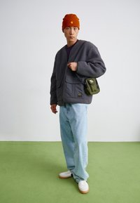 Grå fleece cardigan, lilla skjorte, lyseblå jeans, hvide sneakers med gummisål, orange hue, grøn crossbody taske med lynlåse.