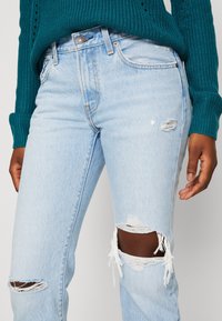 Světle modré džíny z denimu s roztrhnutými koleny a přiléhavým střihem. V kombinaci s texturovaným svetrm v teal barvě.