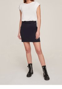 Woman wearing a white short-sleeve top, black mini skirt with belt detail, and black lace-up combat boots, standing against a plain background.