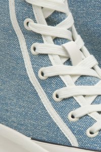 Denim sneaker met een blauwe stoffen bovenkant, witte veters en ronde oogjes. Kenmerkt zich door een witte rubberen zool en contrasterende stikseldetails.
