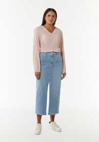 Lichtroze blouse met lange mouwen en een V-hals, gecombineerd met hoge lichtblauwe denim culottes en witte sneakers. Minimalistisch ontwerp.
