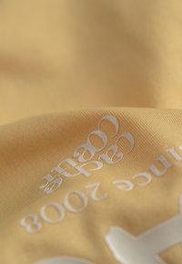 Tissu jaune avec une surface texturée, comportant un texte imprimé en blanc. Le design inclut des chiffres et des lettres stylisés.
