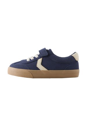 Scarpa da ginnastica in tela blu navy con lacci bianchi e cinturino in velcro. Realizzata con suola in gomma beige e un accento angolare color crema sul lato.