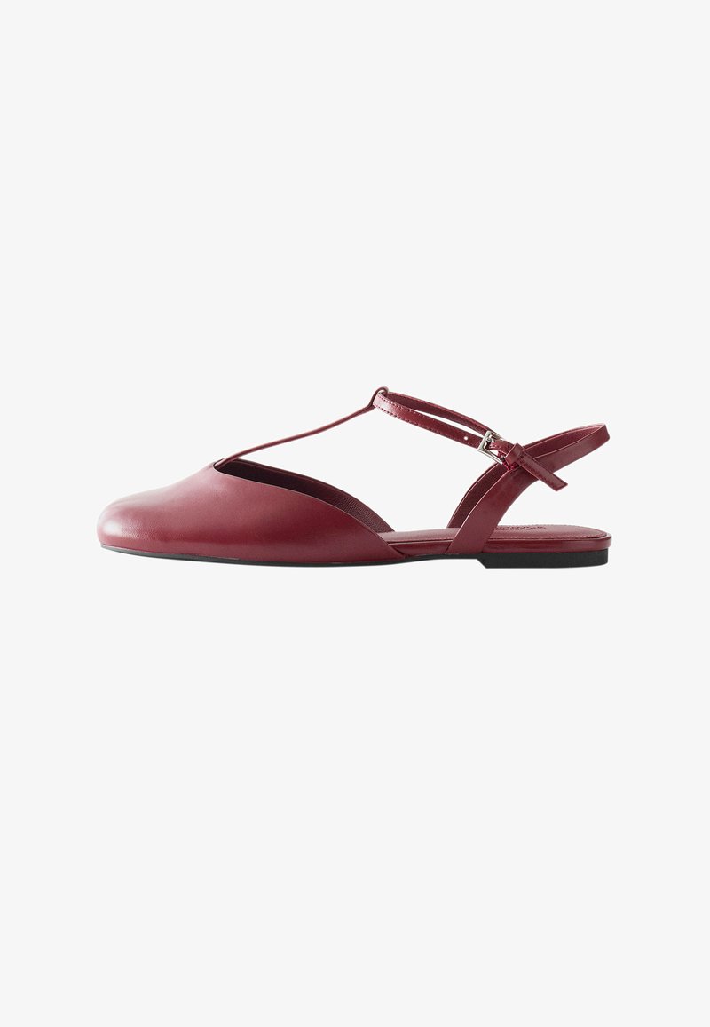 Sandale plate en cuir bordeaux avec bride en T et boucle argentée sur fond blanc.