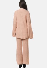 Rosa stickad loungewear-set bestående av en löst sittande cardigan och vida byxor med ribbad textur och långa ärmar.