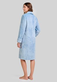Bata de color azul claro hecha de un tejido texturizado con un patrón tejido. Presenta un collar y mangas largas, alcanzando una longitud hasta la mitad de la pantorrilla.