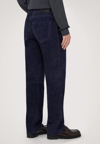 Mörkblå mockabyxor med rak passform, utrustade med fem fickor och förstärkt sömnad. Kombinerade med bruna läderloafers.