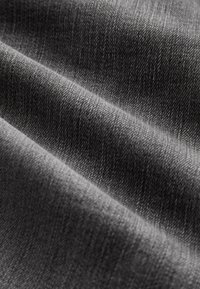 Gros plan d'un tissu gris foncé avec une texture de tissage diagonale visible et des plis doux créant des ombres et des reflets.