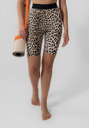 Leopard print bike shorts with a black elastic waistband. A rolled yoga mat secured with an orange strap is held in one hand.