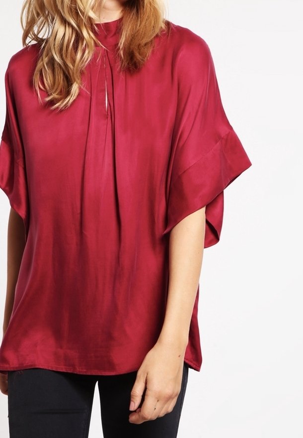 Burgundy silkes blus med hög hals, korta vida ärmar och en nyckelhålsdetalj framtill. Slät textur med en subtil lyster.