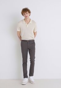 Polohemd in hellem Beige mit strukturiertem Strick, kombiniert mit dunkelgrauen Slim-Fit-Hosen und weißen Sneakern mit beigen Akzenten.