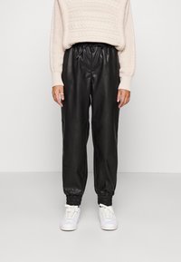 Black leather jogger pants with an elastic waistband and cuffs, paired with a cream knitted sweater. White sneakers complete the look.