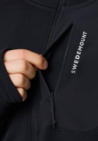 Black zippered jacket with a smooth texture and a visible zippered pocket. "SWEDEMOUNT" logo in white on the right side.