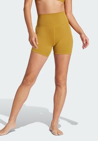 Shorts taille haute de couleur jaune moutarde, avec une texture lisse, présentant un design ajusté et des coutures plates. Pas de motifs ni de pièces métalliques visibles.