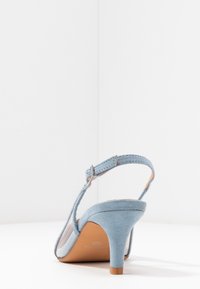 Sandale à talons hauts en nubuck bleu clair avec une sangle à boucle et une semelle beige, vue de l'angle arrière sur fond blanc.
