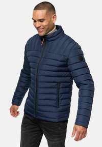 Navy puffer jacket with horizontal quilted design, high collar, orange zipper detail, and side pocket. Smooth fabric texture.