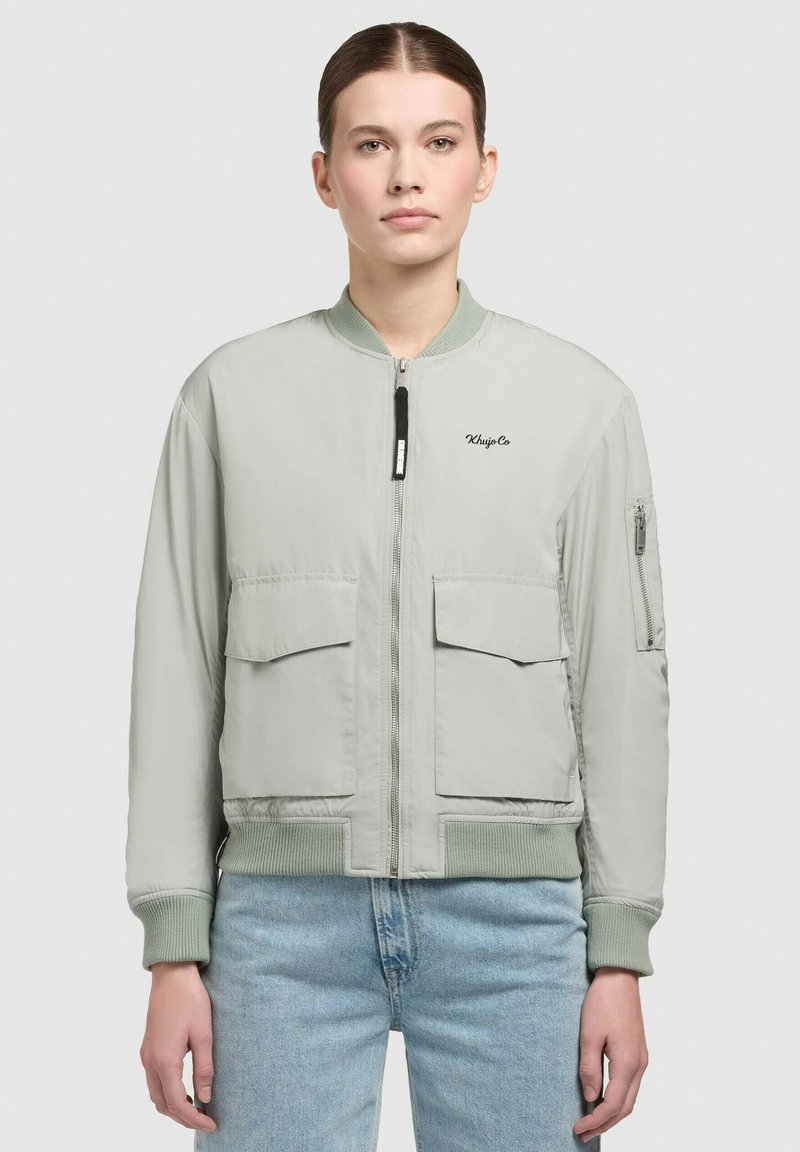 Jachetă bomber gri deschis cu manșete și tiv ribbed, fermoar frontal, două buzunare mari în față și un buzunar lateral. Branding pe piept.