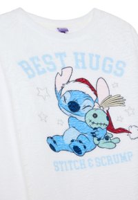 Tessuto bianco e soffice con un design ricamato di Stitch che abbraccia Scrump. Il testo recita "BEST HUGS" in azzurro chiaro, con stelle.