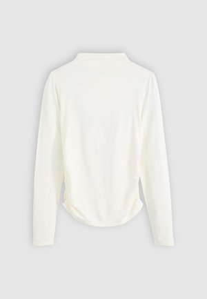 Top de manga larga en tejido color crema, con un ligero fruncido a los lados y un cuello clásico. Textura suave, diseño sencillo.
