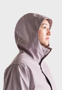 Vodoodpudivá bunda v svetlej levandulovej farbe s priliehavou kapucňou a zipsovým uzáverným systémom. Hladká textúra a minimalistický dizajn, ktorý obsahuje tonálne švy.