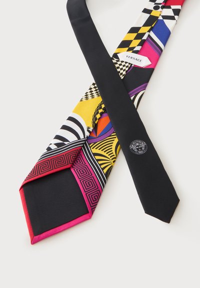 Cravate en soie avec des motifs géométriques colorés, étiquette Versace visible et dos noir avec un logo tête de Méduse brodé près de la pointe.