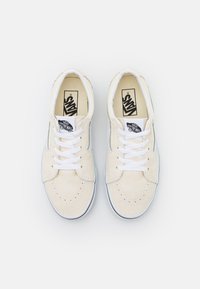 Beige Leinenschuhe mit weißen Schnürsenkeln, perforierter Zehenbox und schwarzem Vans-Logo-Patch. Gummisohle mit grauen Akzenten und hellen Nähten.