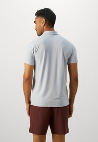 Lys grå polo skjorte med korte ærmer, en blød tekstur, og en klassisk krave, parret med maroon shorts. Ingen synlige logoer eller mønstre.