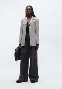 Γκρι υφασμάτινο σακάκι με υφή, μαύρο τοπ, φαρδιά σκούρα παντελόνια, μαύρη τσάντα και επίπεδα παπούτσια· διαθέτει ένα κουμπί και πέτο με σχισμή.