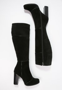 Svarta stövlar av mocka som når över knäna. Har en hög klack och dragkedjedetalj på sidan för enkel påtagning.
